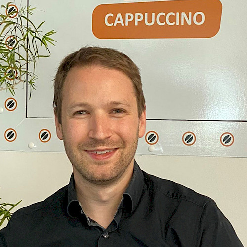Christoph Schaffer, Head of Digital Energy Solutions, bei „Auf einen Kaffee mit...“-Interview, vor Cappuccino-Schild im modernen Büro.